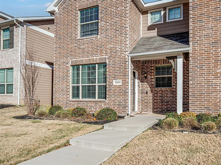 Two-story brick and siding townhome featuring a covered entry, gabled rooflines, multiple windows, and a concrete pathway