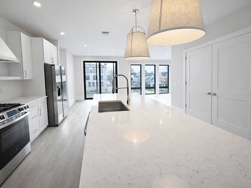 Modern chef's kitchen with quartz waterfall island, custom white cabinetry, and stainless steel appliances. Gas range, wall oven, tile backsplash, and designer pendant lighting. Bright, open layout with abundant natural light_ideal for cooking and enterta