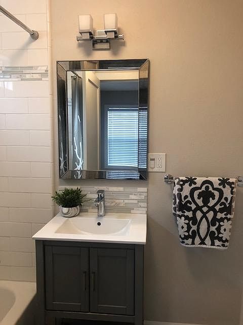 Beautifully remodeled bathroom. White subway tile bath/shower surround, marble/glass accents, gray maple shaker vanity, porcelain integrated sink, gray tile floors, window in bathroom.