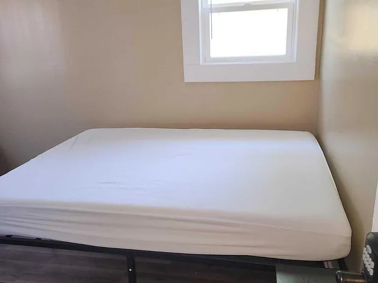 Compact bedroom with neutral walls, durable wood-style flooring, and a window for natural light above the bed area.