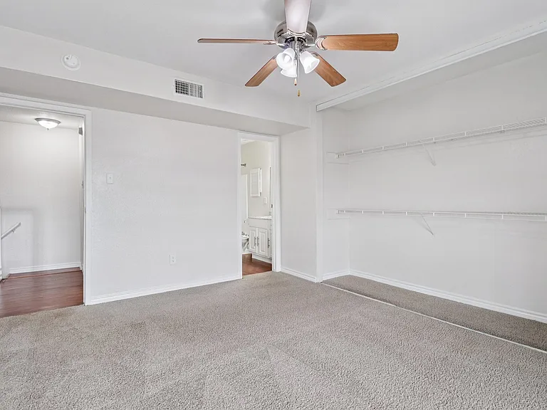 Bright and inviting bedroom with plush carpet, ample closet shelving, and a ceiling fan, offering comfort and style. Bright and inviting bedroom with plush carpet, ample closet shelving, and a ceiling fan, offering comfort and style.