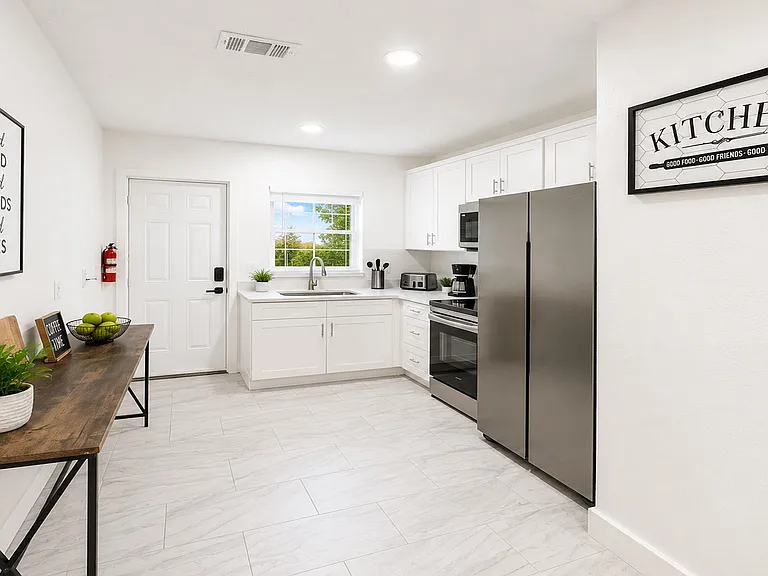 Efficient kitchen with white cabinetry, stainless steel appliances, and a window over the sink plus space for a small table.