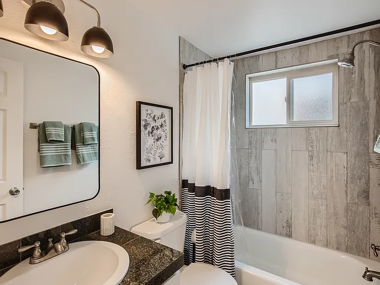 The updated bathroom features an all new vanity, light fixture, modern mirror, and trendy tile surround in the tub/shower combo.