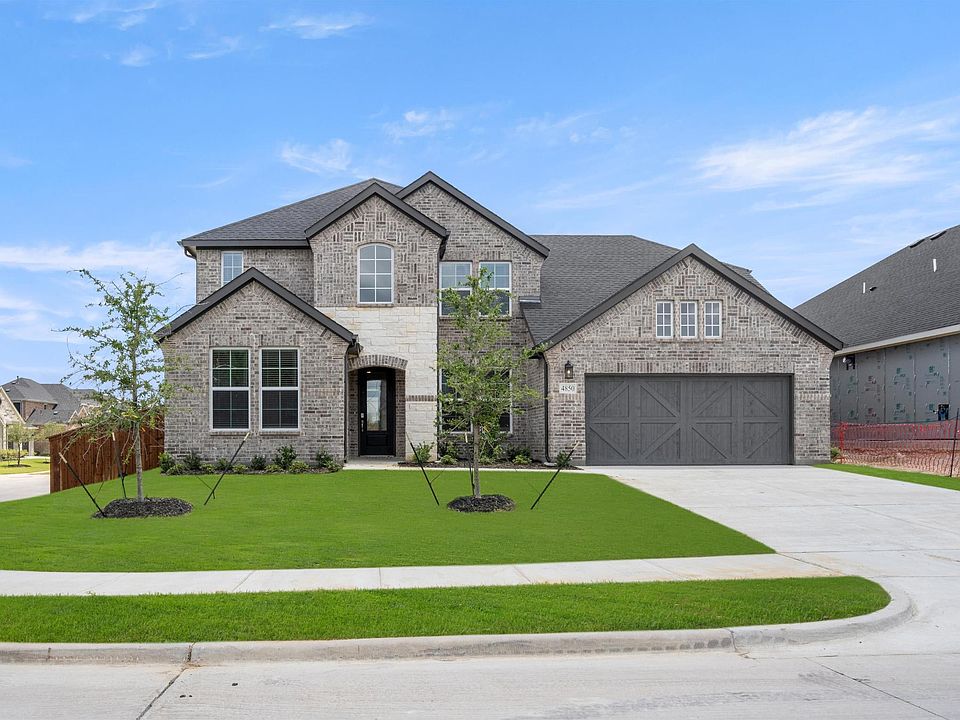 A two-story brick and stone house with a garage, surrounded by a well-manicured lawn and landscaping