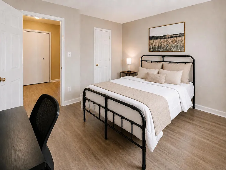 Furnished bedroom featuring a full bed, nightstand with lamp, and dedicated desk space with convenient closet access.