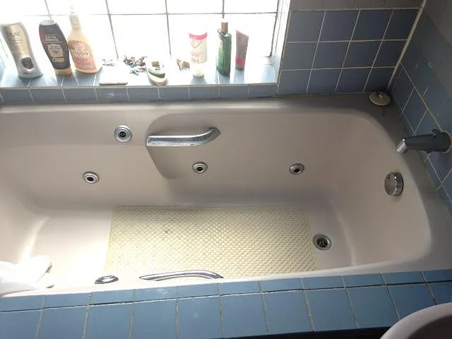 Large jetted bathtub with handles. Glass brick window/wall