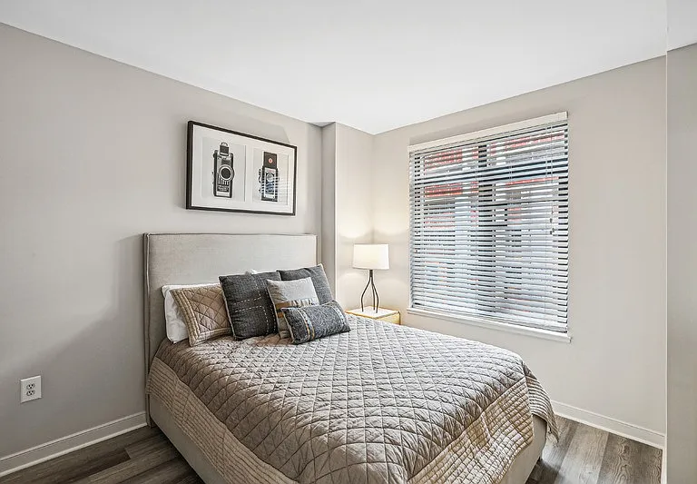 Bedroom with Bed, Lamp, and Window Blinds Overlooking Exterior