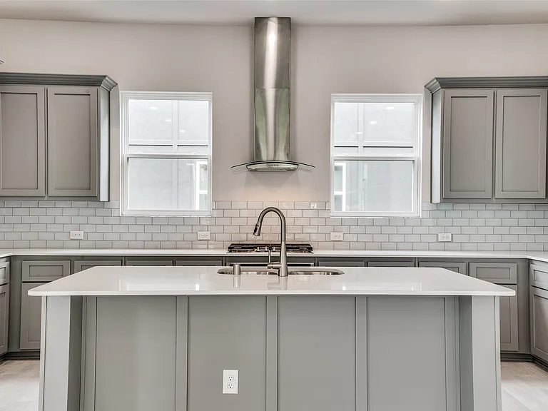 Double sinks in island with dishwasher, built-in microwave, gas cooktop with vent above and oven below and windows that have blinds (not shown)