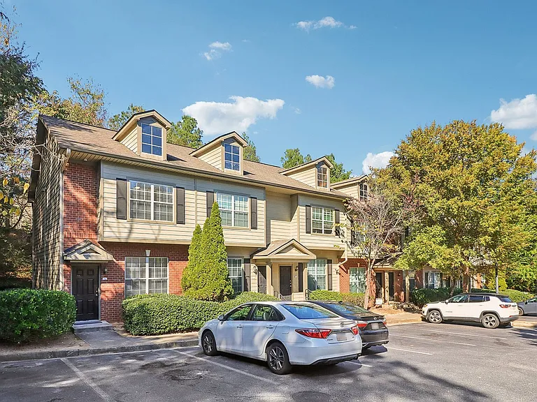 Charming townhouse exterior surrounded by lush greenery, featuring modern architecture with dormer windows and ample parking space.