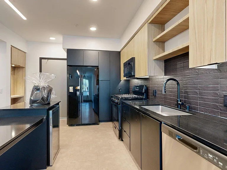 Apartment kitchen with black appliances, dark counters, and tile floor.