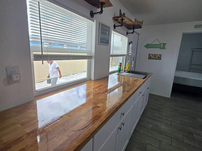 Galley-style kitchen with long butcher-block counters, ample cabinetry, open wood shelving, and a stainless sink.