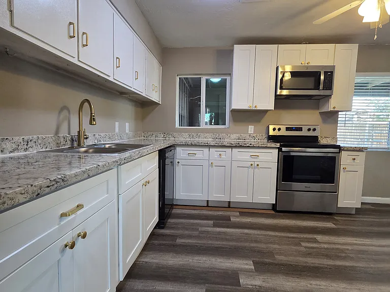 This view of the kitchen allows you to see the cabinets a bit closer. Gold-tone faucet and cabinet hardware. Electric stove-top and oven.