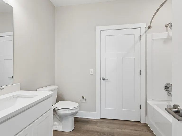 Bathroom with quartz countertops, closet, and bath/shower of an apartment unit.