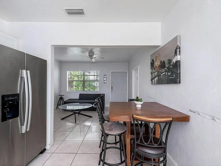 Dining area with a pub-height table set beside an open living space, plus tiled floors and a large window for daylight.