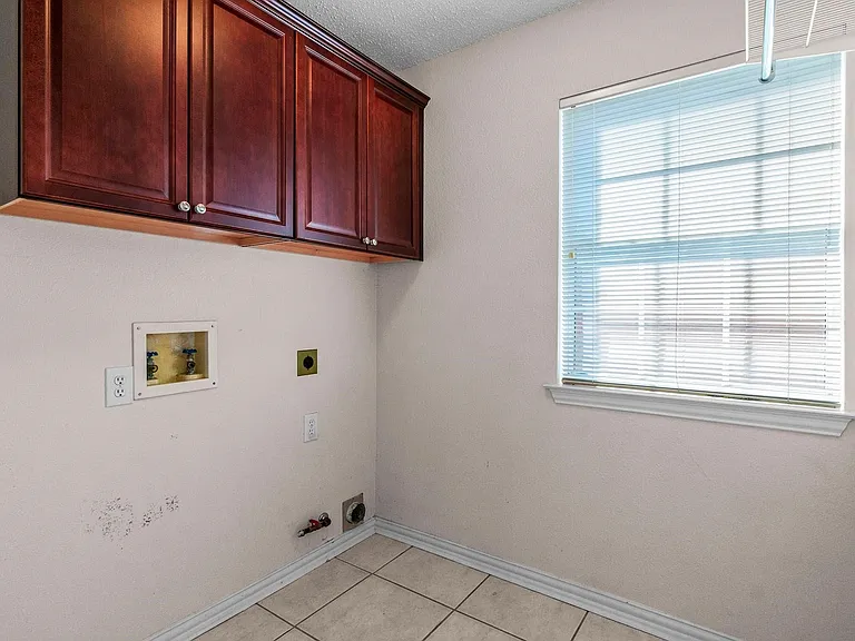 Laundry area featuring upper cabinetry with panel doors, a window with horizontal blinds, and tiled flooring