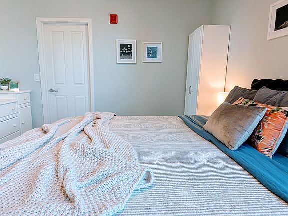luxurious California king size plush bed. White door leads to hallway, bathroom just to the left in hallway