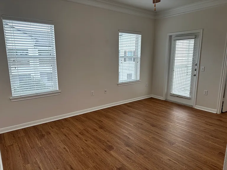 Bright room with elegant wood-style flooring, white walls, large windows, and a glass door, perfect for a cozy apartment atmosphere. Bright room with elegant wood-style flooring, white walls, large windows, and a glass door, perfect for a cozy apartment a
