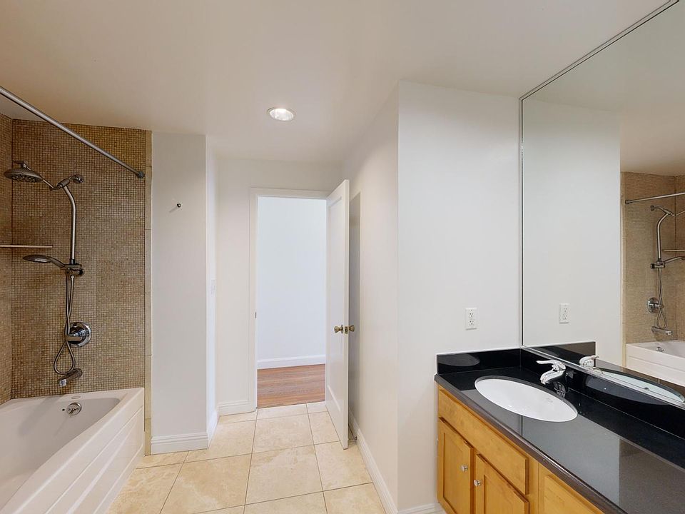 Bathroom featuring a bathtub, shower with tiled wall, double sink vanity, and a doorway leading to another room