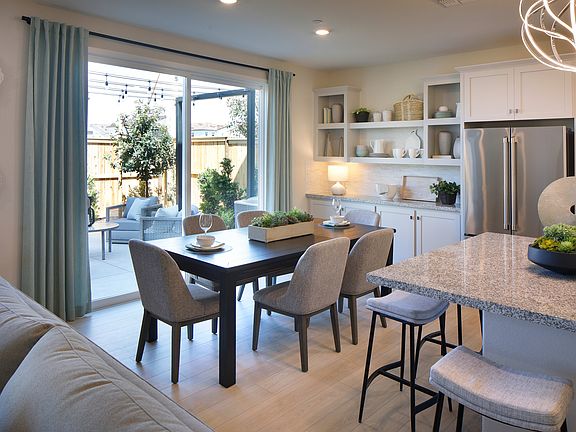 A modern and cozy kitchen-dining area with a large window overlooking a patio, featuring a wooden di