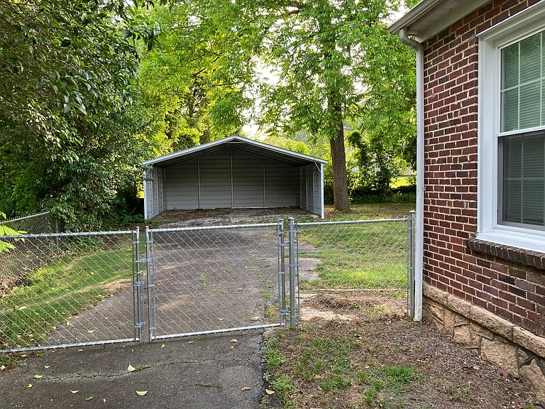 Large, fenced in backyard with 2 car carport and storage building behind carport.