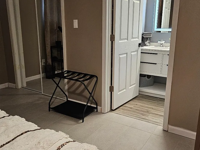 Luggage rack in bedroom between closet and bathroom entrance.