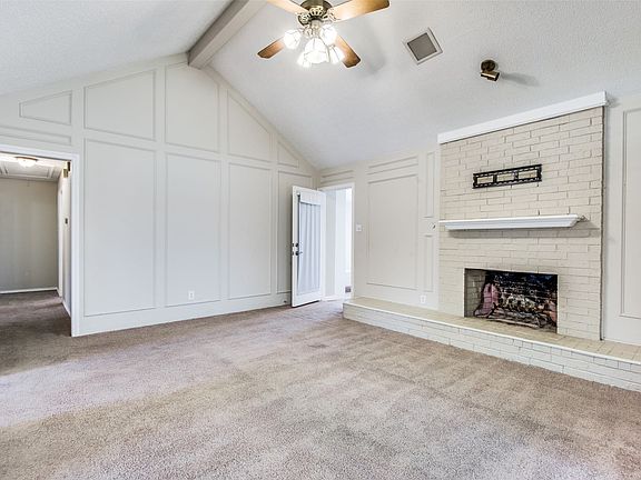 Living room featuring a vaulted ceiling with a ceiling fan, a painted brick fireplace with a mantel, and paneled wall details