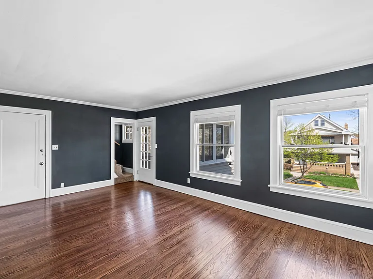 This photo shows the front entrance to the home, entering in the living room, as well as the door that leads to the sunroom and steps that lead to the third floor.