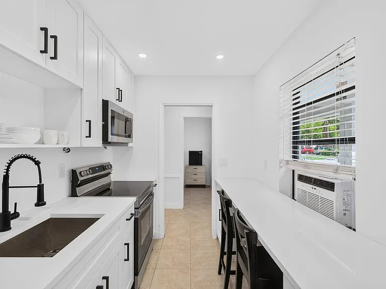 Galley kitchen with shaker cabinets, stainless range and microwave, and a long breakfast bar beside the window.