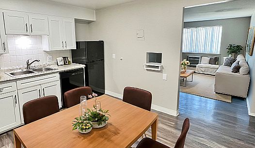 Inviting apartment kitchen and dining area with modern white cabinetry, cozy dining table, and view into a bright living room with stylish decor.