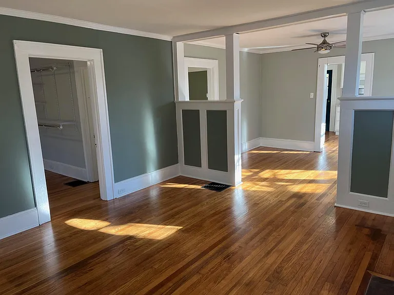 View of living room. Nearest door is to largest bedroom. Door behind half wall opens to the hallway with access to the front bedroom, full bathroom and middle bedroom. Doorway on the farthest wall in image is to the kitchen.