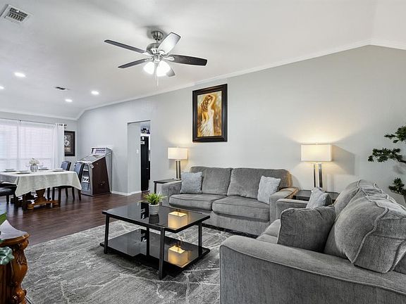 Living room with ceiling fan, vaulted ceiling, ornamental molding, and dark wood-type flooring