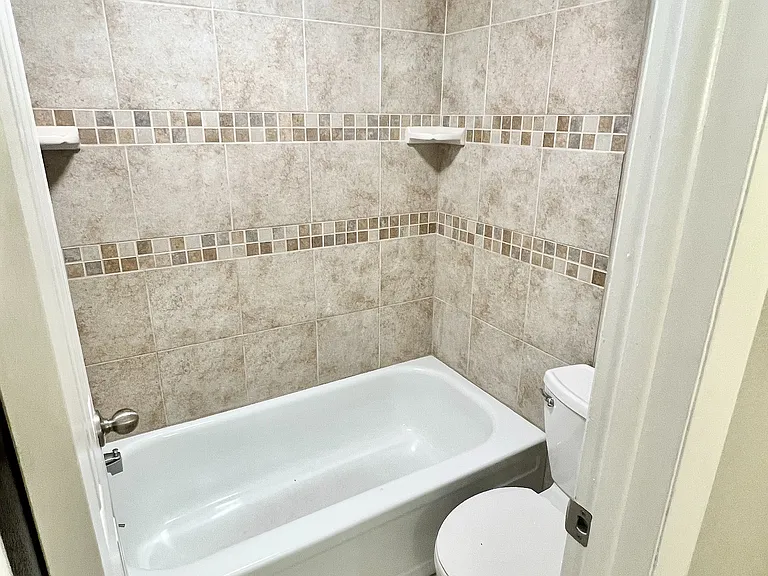 Elegant bathroom showcasing modern beige tile, a cozy bathtub, and a clean, minimalist design.