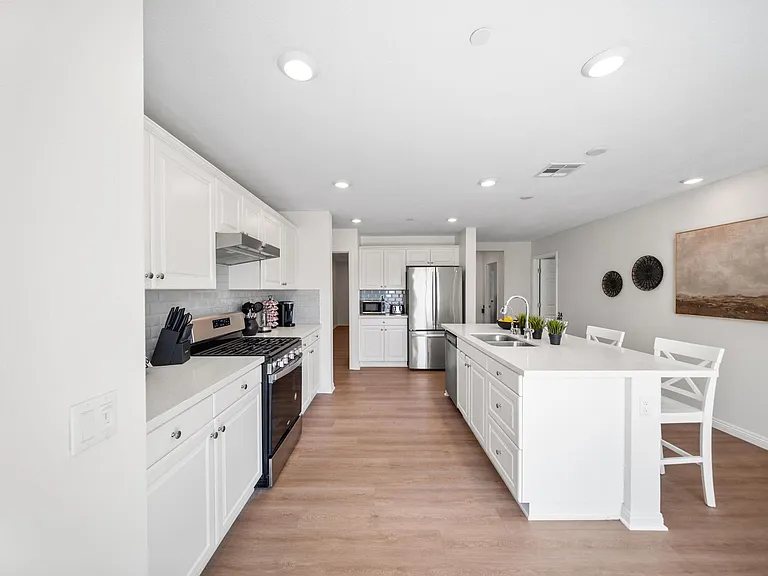 Spacious kitchen with ample white cabinetry, stainless steel appliances, and a large island with seating and sink.
