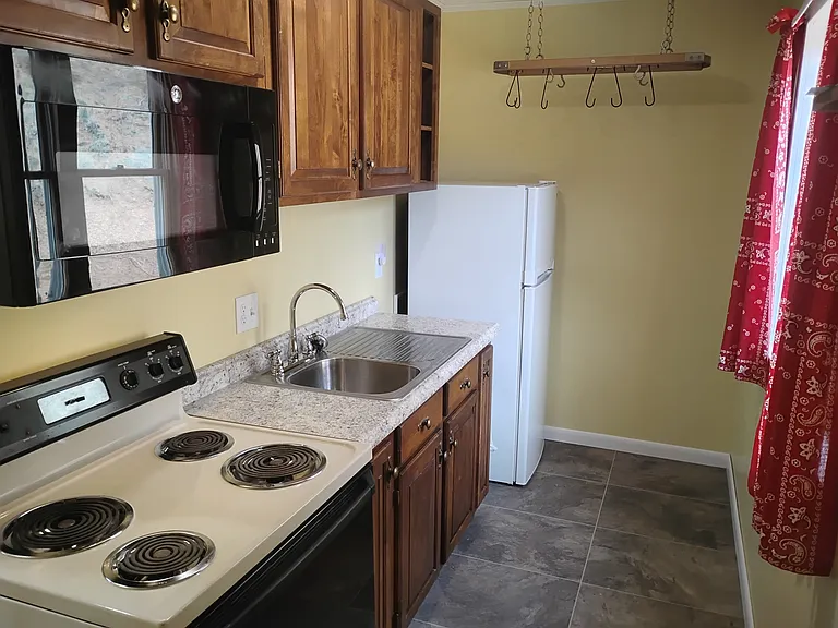 Four-burner stove, microwave, deep kitchen sink, new fridge, hanging pot rack. There is a window in the kitchen.