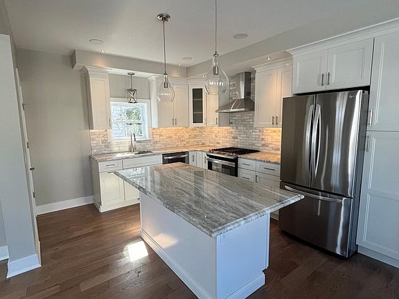 Kitchen with marble countertop and stainless steel appliances including gas range, dishwasher, microwave, range hood and fridge with ice maker
