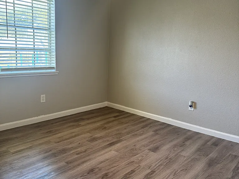 This bright bedroom offers clean gray walls, wood_style flooring, and ample natural light enhanced by a modern ceiling fan.