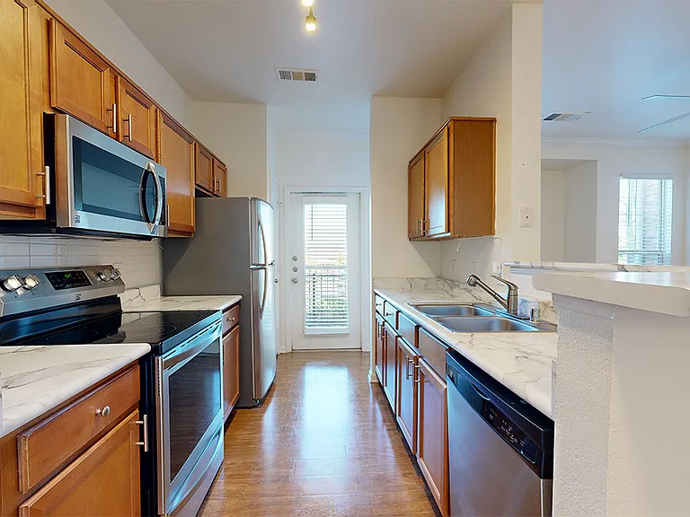 Apartment kitchen with stainless steel appliances, wood-style flooring, and marble-style countertops (shown here). Quartz-style countertops are available in select homes.