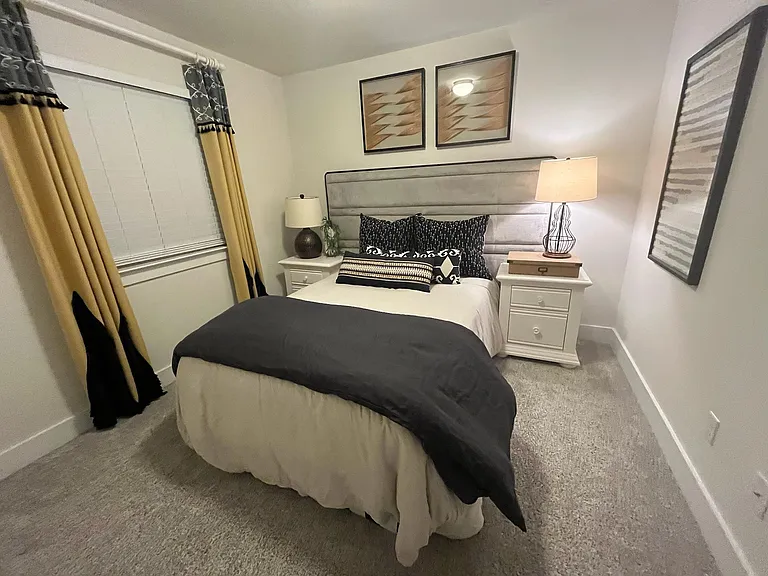 Furnished bedroom with a comfortable bed, two nightstands with lamps, and a window with curtains for privacy.