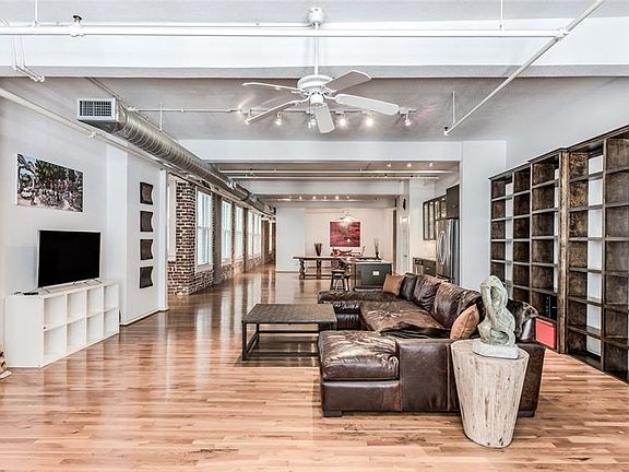 This sprawling loft is sure to impress. Looking through Living, Kitchen, Dining into open Secondary Bedroom where red wall art is. Entry Hall to left where brick starts. Exposed brick hallway to far left leads to Master Suite. Fresh Paint throughout.