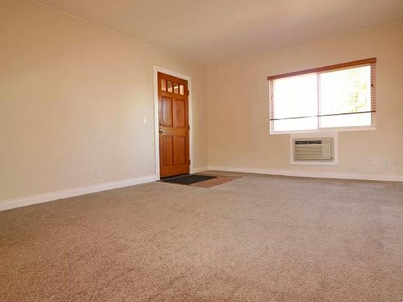 Front door, Living room, and wall A/C unit. Lots of good light and blinded shades for the windows.