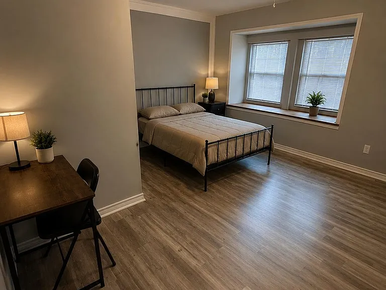 Spacious bedroom with wood-style floors, ceiling fan, and a dedicated desk area, plus a large window ledge for natural light.