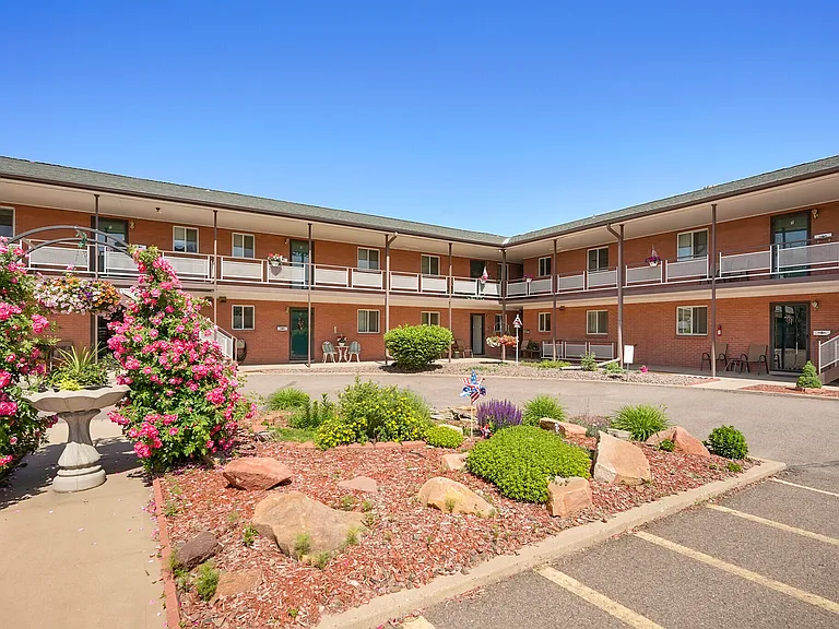 Charming apartment complex with well-maintained gardens and blooming flowers under a clear blue sky.