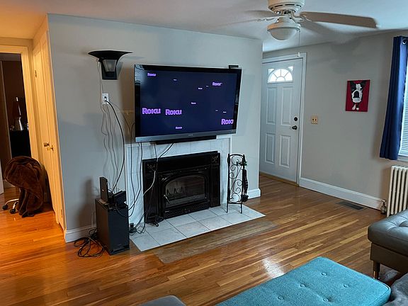 Living room with wood burning fireplace with fan for heating house.
To the left of the photo you can see the doors that lead to the bedroom and another (along the side) that leads to the basement. 
"Front Door" to home is on the right.