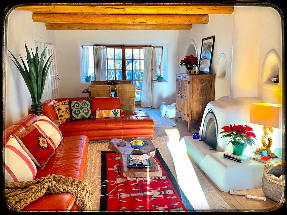 Living room with kiva fireplace, coved spaces, original hardwood floors and viga ceilings. Dining area is to the rear of photo w/ 2nd deck off it.