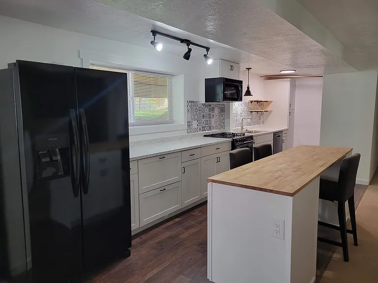 Downstairs newly remodeled kitchen with butcher block breakfast bar, plentiful cabinet and drawer storage, and wide countertops. Kitchen features gas range, microwave, dishwasher, garbage disposal, and water and ice in 2-year-old fridge.