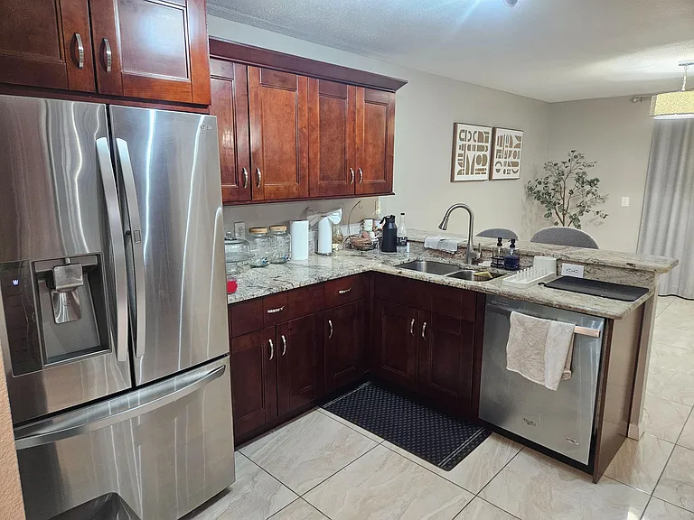 Open kitchen with granite countertops, ample wood cabinetry, and stainless-steel refrigerator and dishwasher plus breakfast b