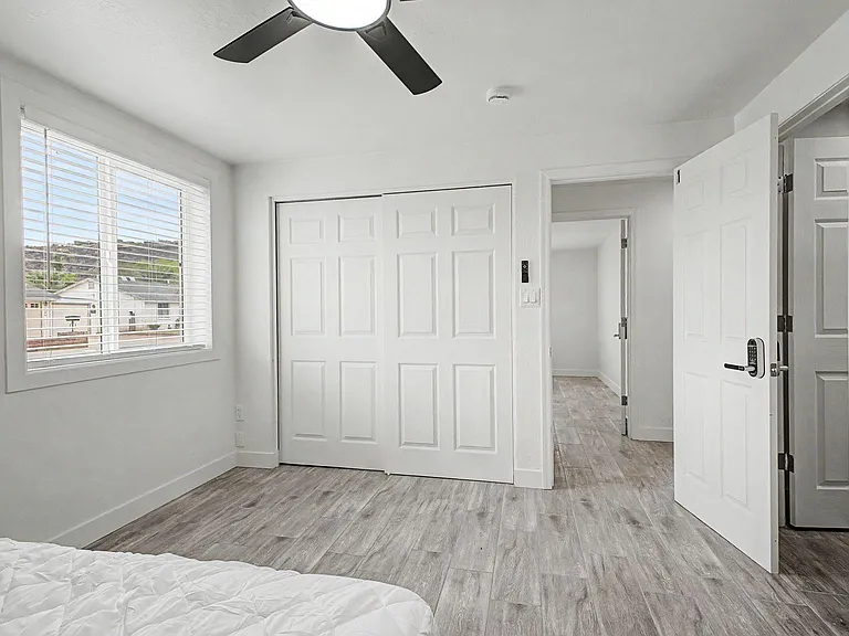 Bedroom with wide window, ceiling fan light, and spacious double-door closet, plus durable wood-look flooring.