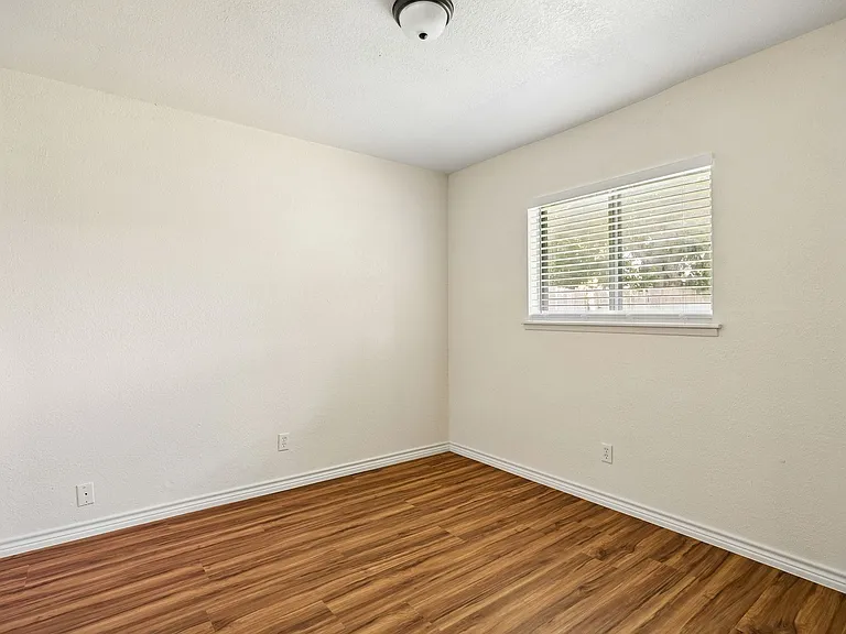 Room featuring wood-finish flooring, neutral wall tones, window with horizontal blinds, and a flush-mount ceiling light fixture