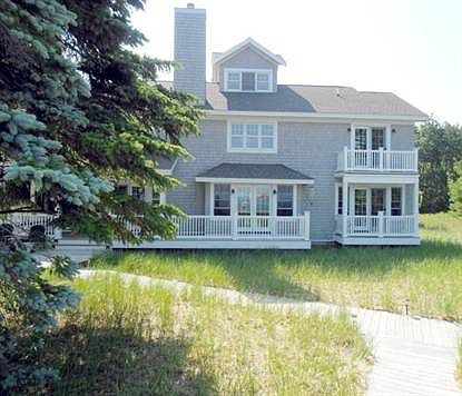 Lakeside aspect of home as it appears to float above the beach grass landscape. South end bedroom suites on both levels have private decks with great views.  Main level deck unifies entertainment, dining & screen porch spaces as well as accessing west patio, walkways & lakeside deck with firepit.