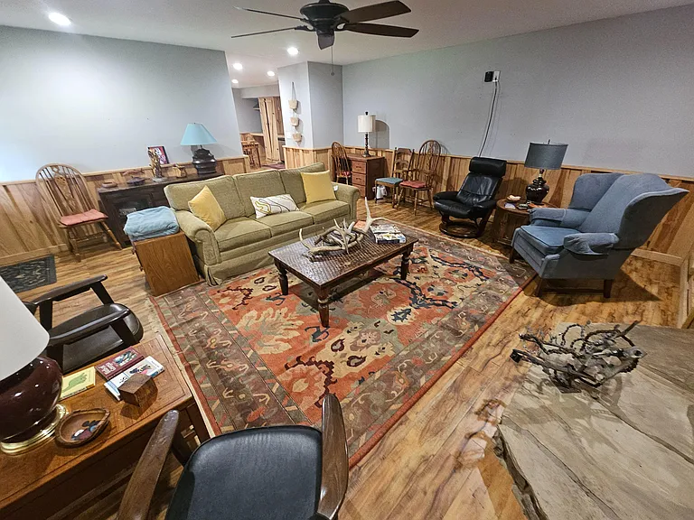 Spacious shared living room with multiple seating areas, ceiling fan, and warm wood floors anchored by a large area rug.